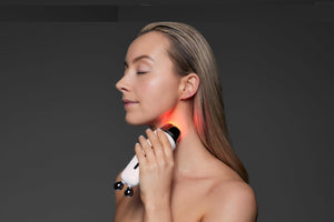Sculpta by Déesse PRO facial rejuvenation device in white with black accents, emitting red light on a woman's neck.